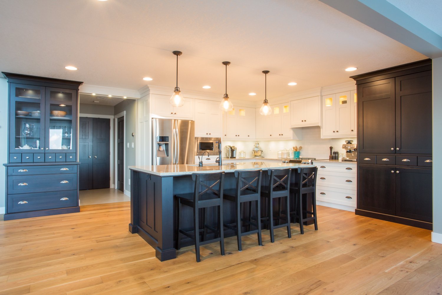 L-shaped kitchen with light and dark cabinets, stainless appliances, hardwood floors and an island in the center with stools 